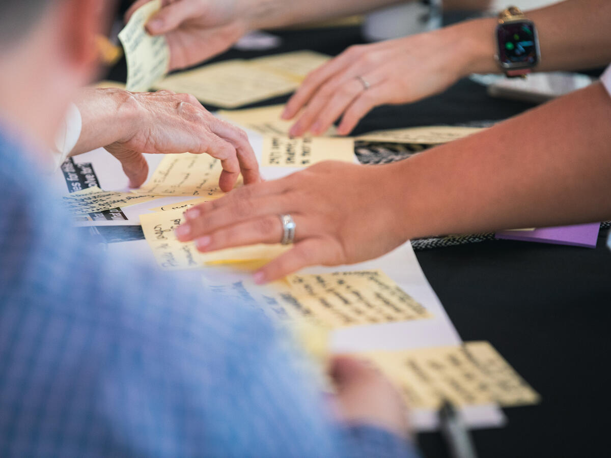 multiple hands reaching over a table and placing sticky notes